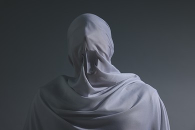Photo of Creepy ghost. Man covered with white sheet on light grey background