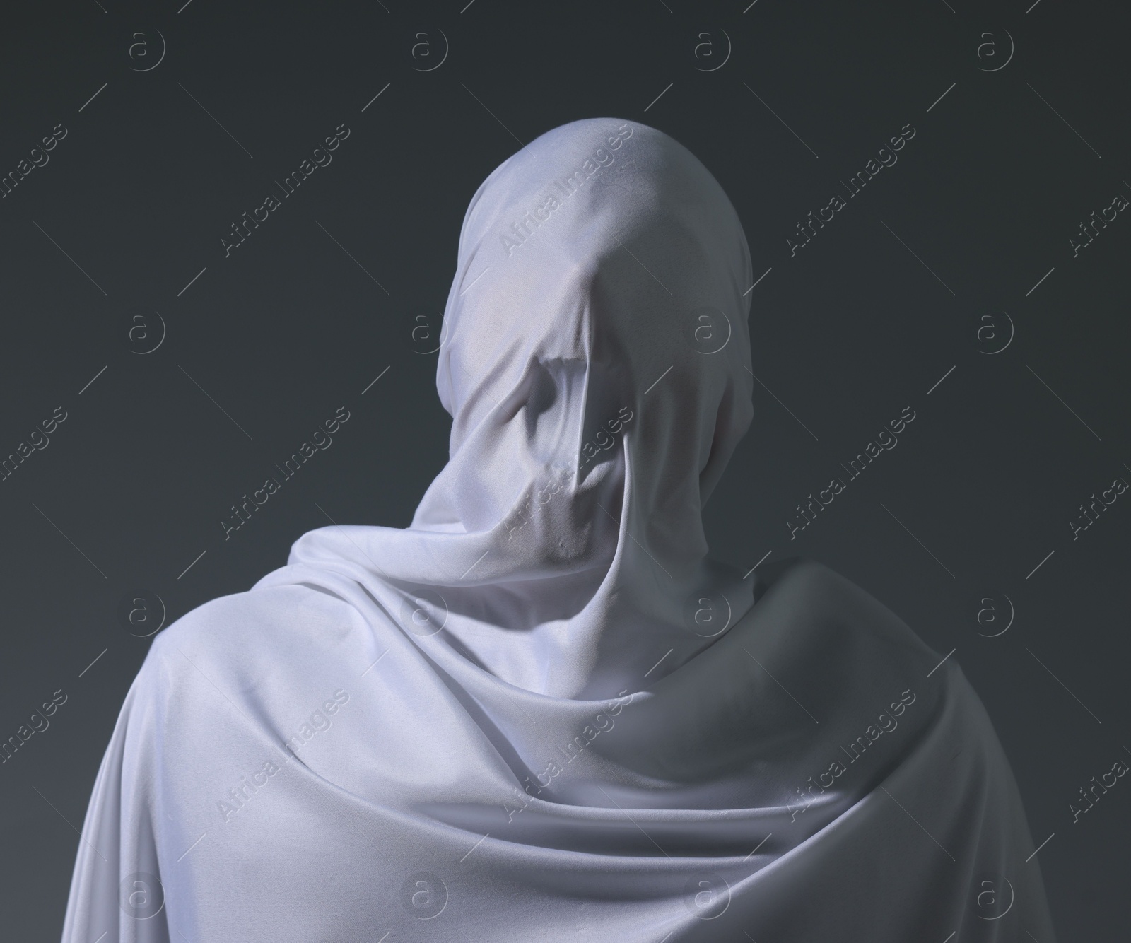 Photo of Creepy ghost. Man covered with white sheet on light grey background