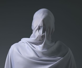 Photo of Creepy ghost. Man covered with white sheet on light grey background