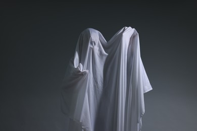 Photo of Creepy ghost. Man covered with white sheet on light grey background