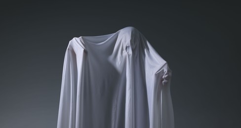 Photo of Creepy ghost. Man covered with white sheet on light grey background