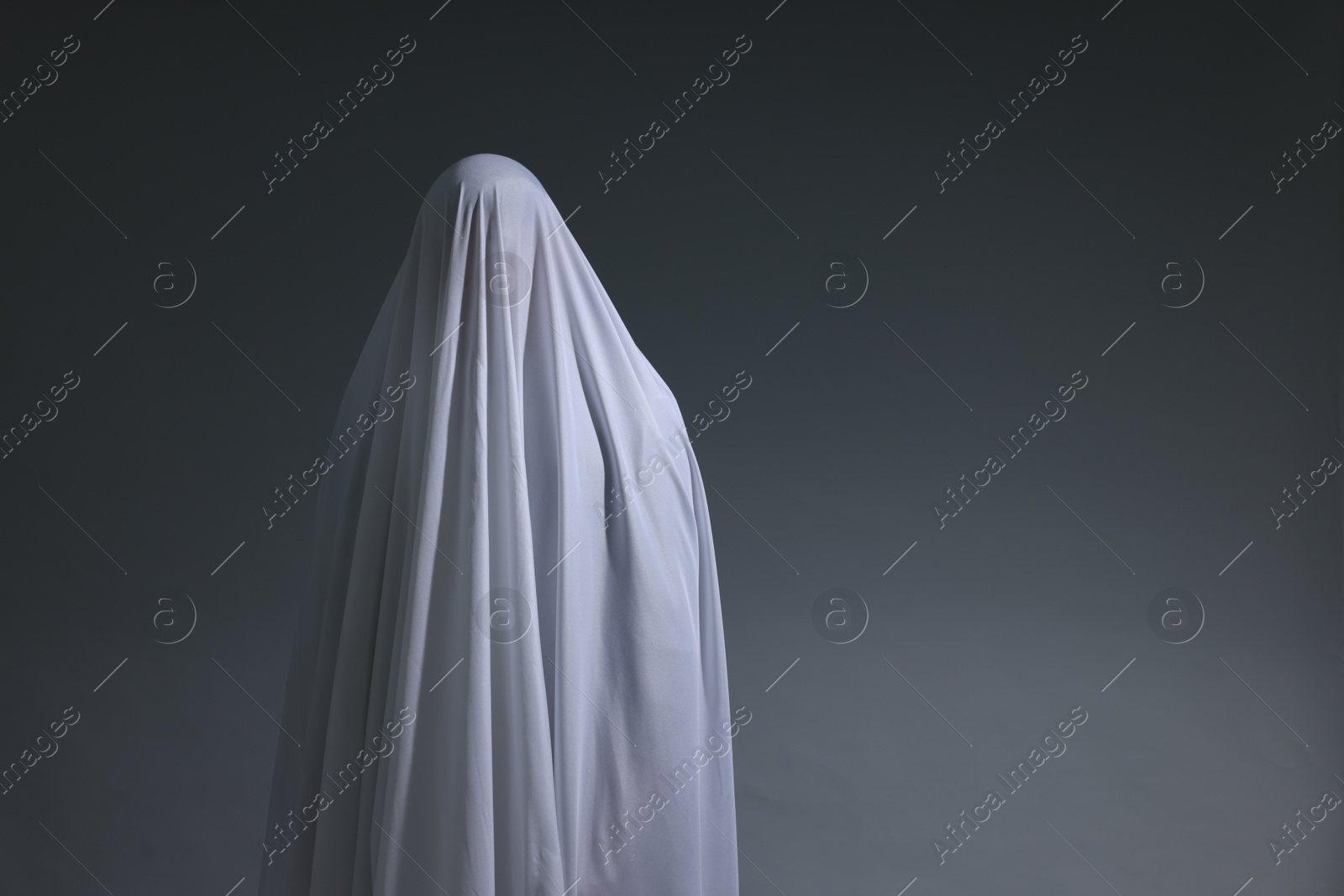 Creepy ghost. Man covered with white sheet on light grey background, space for text Photo of Creepy ghost. Man covered with white sheet on light grey background, space for text