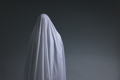 Photo of Creepy ghost. Man covered with white sheet on light grey background, space for text