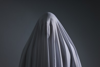 Photo of Creepy ghost. Man covered with white sheet on light grey background