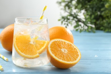 Photo of Sparkling water with orange slices in glass and fresh fruits on light blue wooden table, closeup. Space for text