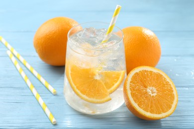 Photo of Sparkling water with orange slices in glass, fresh fruits and straws on light blue wooden table, closeup