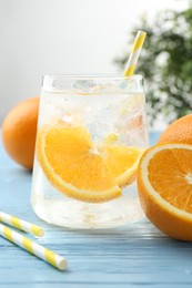 Photo of Sparkling water with orange slices in glass, fresh fruits and straws on light blue wooden table, closeup