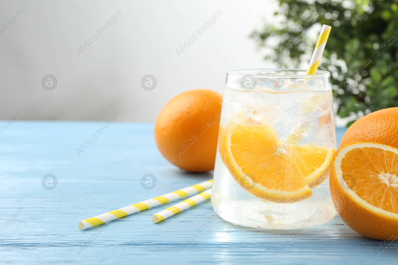Photo of Sparkling water with orange slices in glass, fresh fruits and straws on light blue wooden table, closeup. Space for text