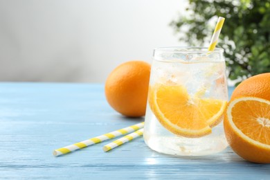 Photo of Sparkling water with orange slices in glass, fresh fruits and straws on light blue wooden table, closeup. Space for text