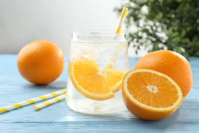 Photo of Sparkling water with orange slices in glass, fresh fruits and straws on light blue wooden table, closeup