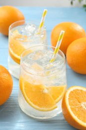 Photo of Sparkling water with orange slices in glasses and fresh fruits on light blue wooden table, closeup