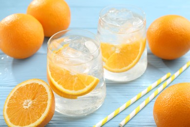 Photo of Sparkling water with orange slices in glasses, fresh fruits and straws on light blue wooden table, closeup