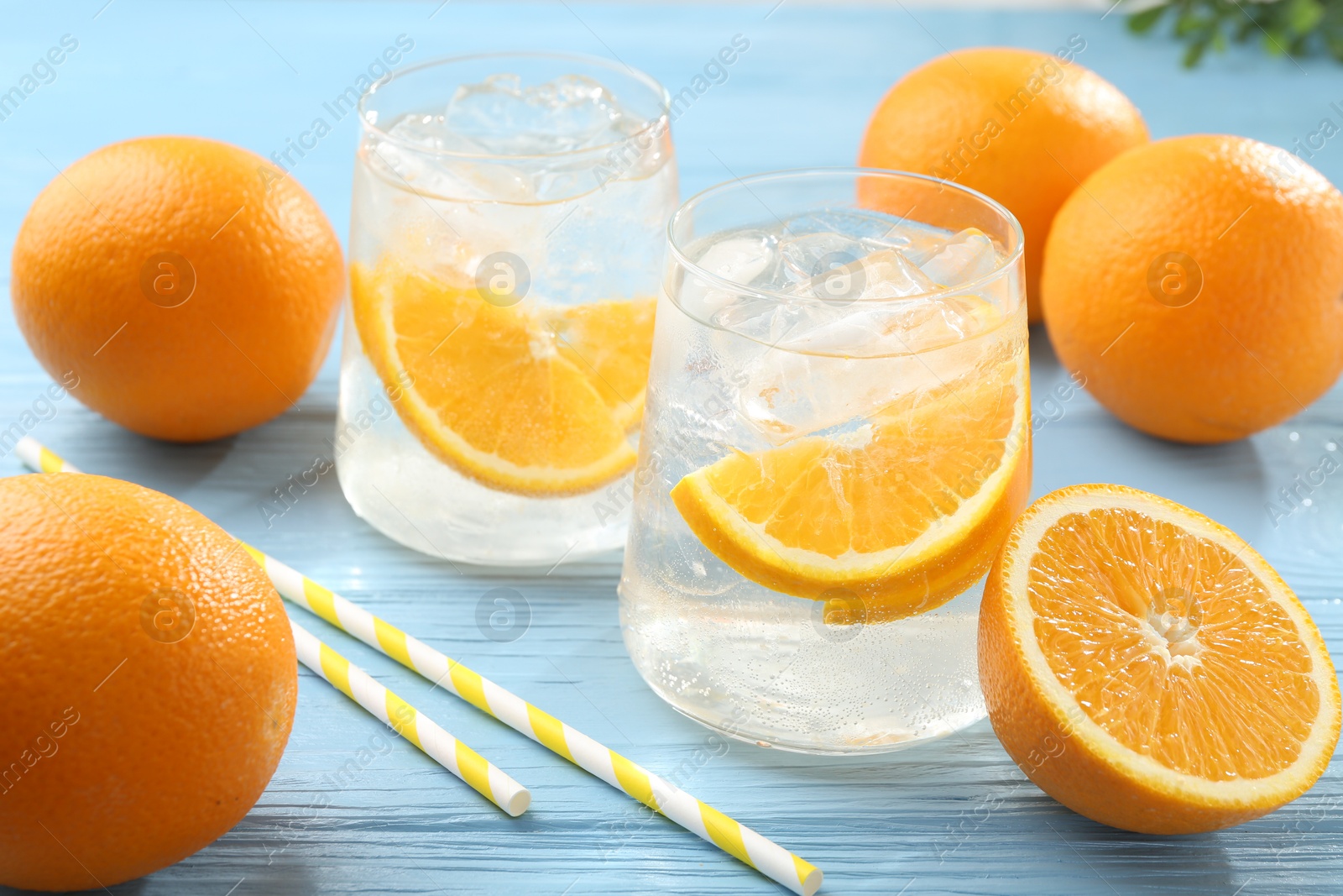 Photo of Sparkling water with orange slices in glasses, fresh fruits and straws on light blue wooden table, closeup
