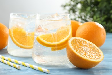 Photo of Sparkling water with orange slices in glasses, fresh fruits and straws on light blue wooden table, closeup