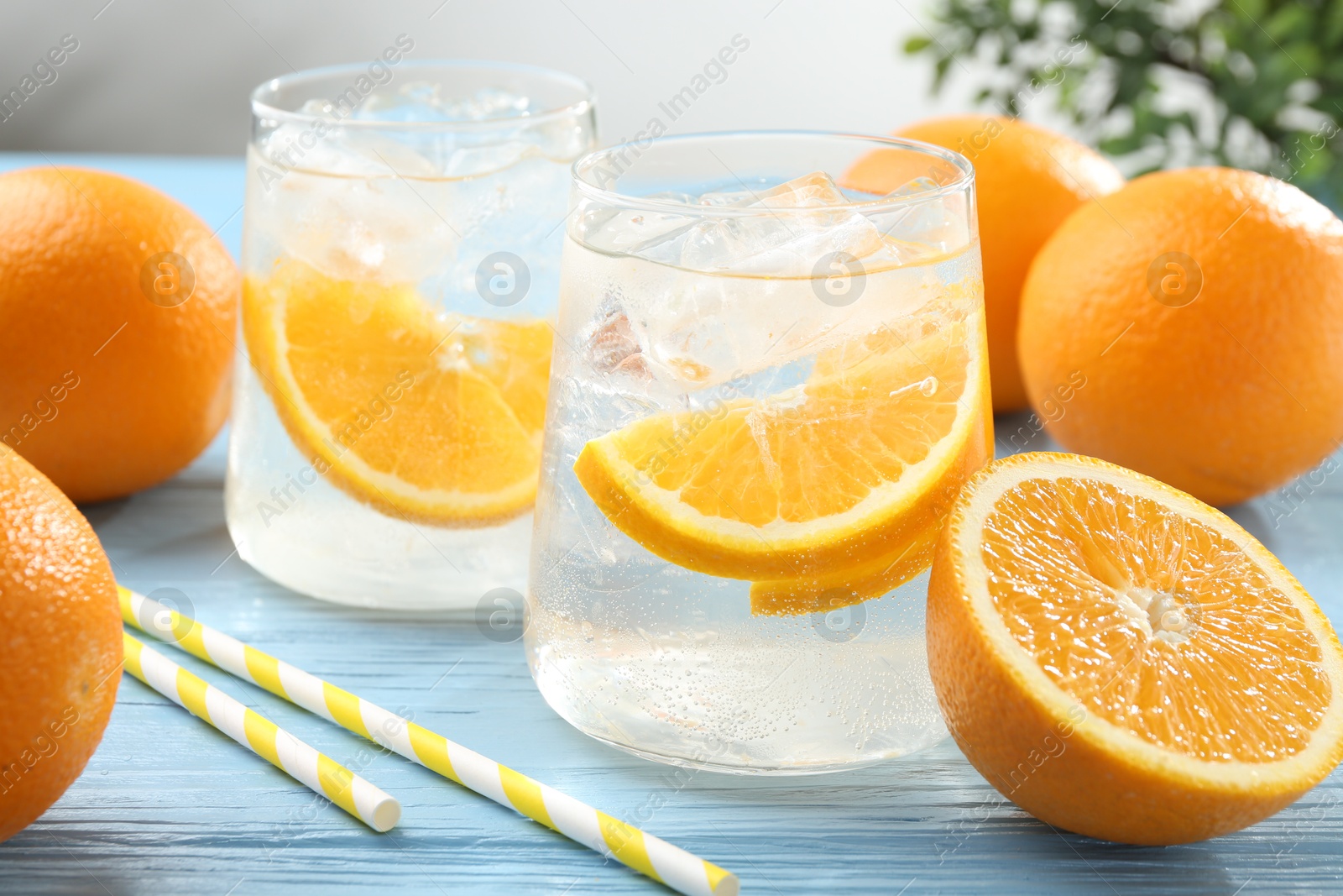Photo of Sparkling water with orange slices in glasses, fresh fruits and straws on light blue wooden table, closeup