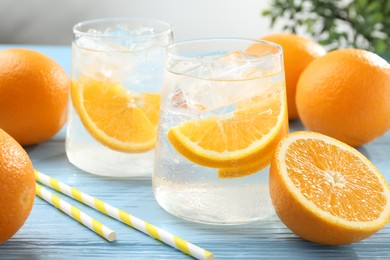 Photo of Sparkling water with orange slices in glasses, fresh fruits and straws on light blue wooden table, closeup