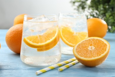 Photo of Sparkling water with orange slices in glasses, fresh fruits and straws on light blue wooden table, closeup
