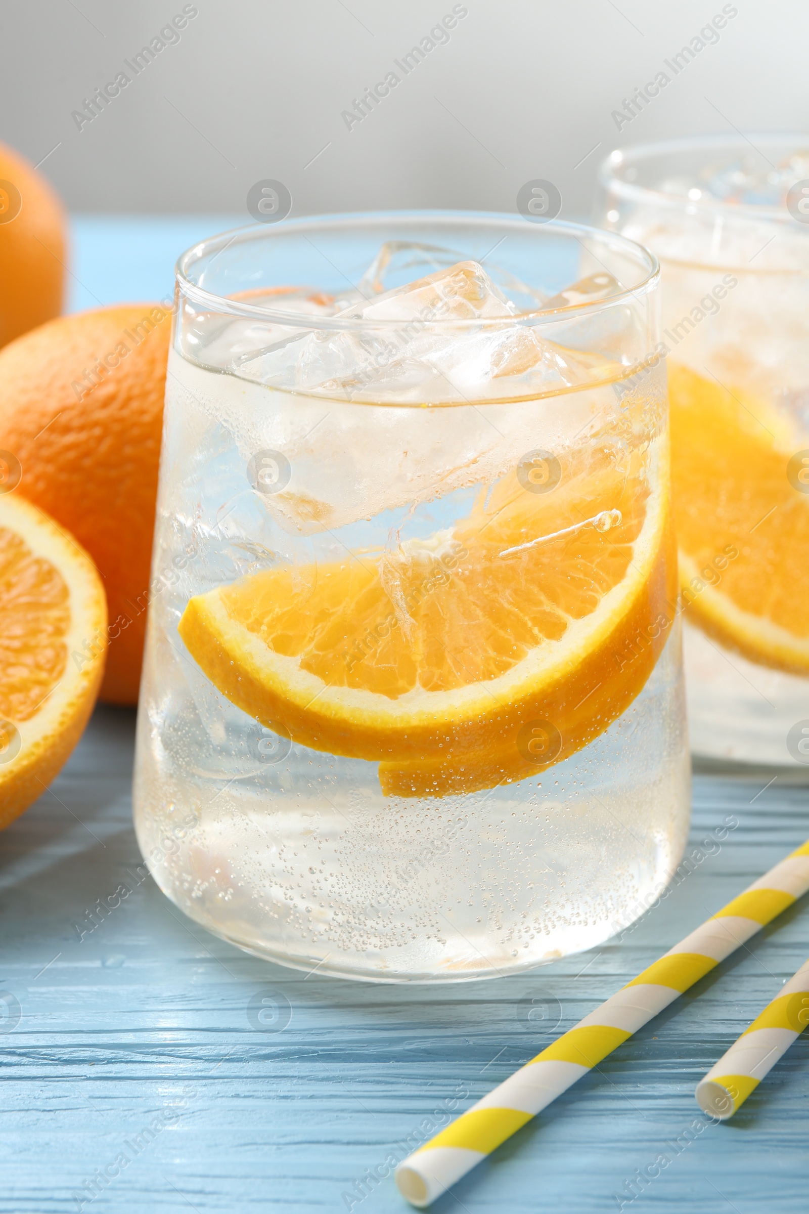 Photo of Sparkling water with orange slices in glasses, fresh fruits and straws on light blue wooden table, closeup