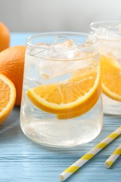 Photo of Sparkling water with orange slices in glasses, fresh fruits and straws on light blue wooden table, closeup