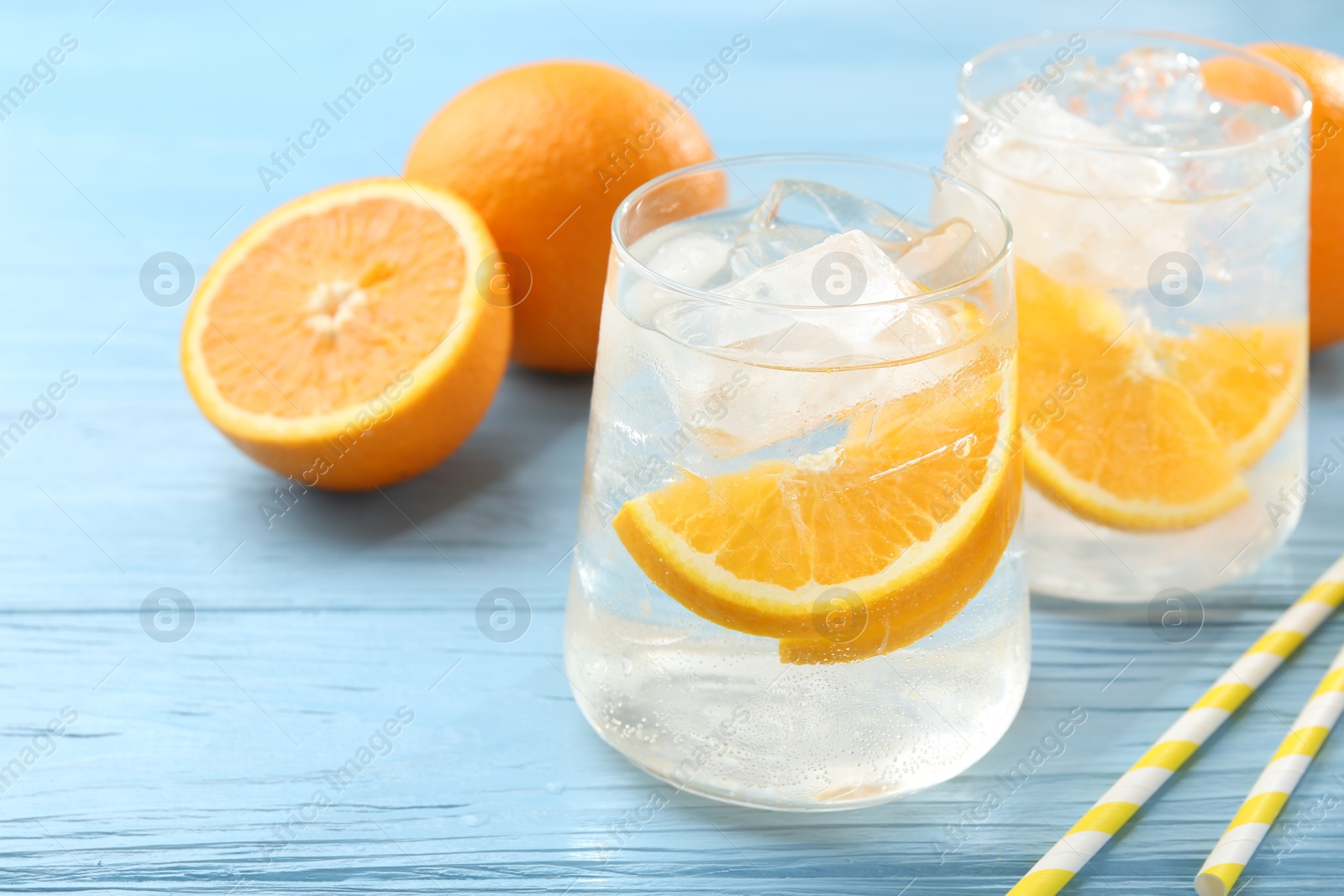 Photo of Sparkling water with orange slices in glasses, fresh fruits and straws on light blue wooden table, closeup