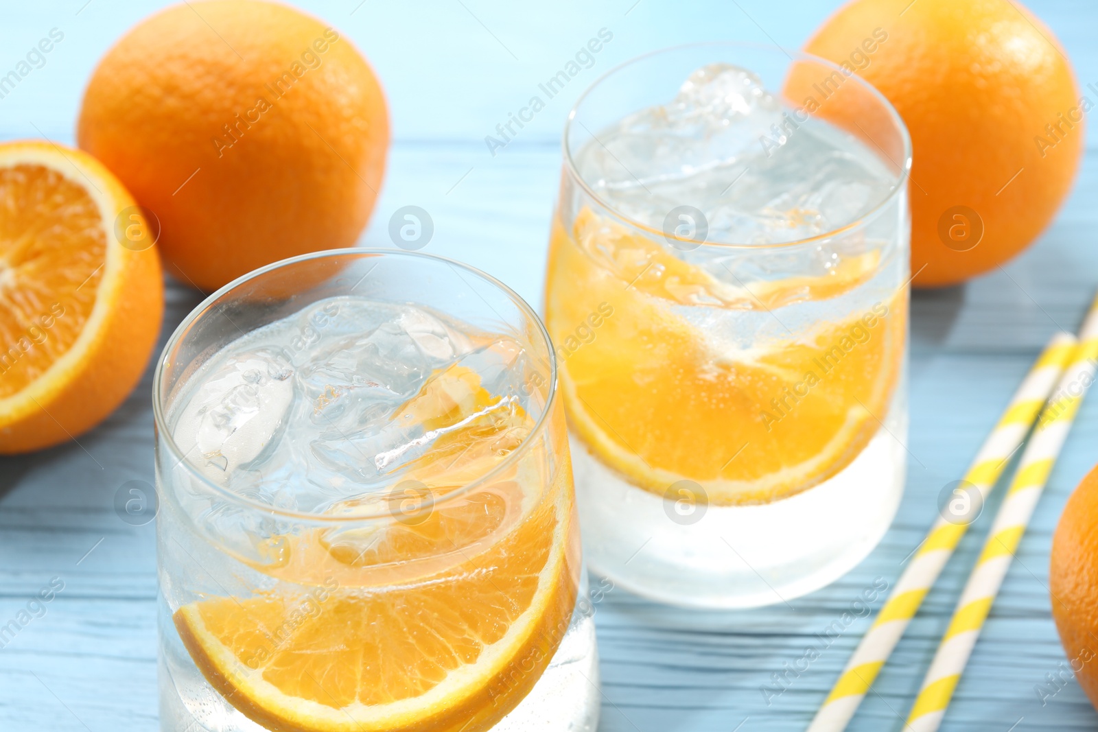 Photo of Sparkling water with orange slices in glasses, fresh fruits and straws on light blue wooden table, closeup