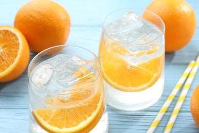 Photo of Sparkling water with orange slices in glasses, fresh fruits and straws on light blue wooden table, closeup