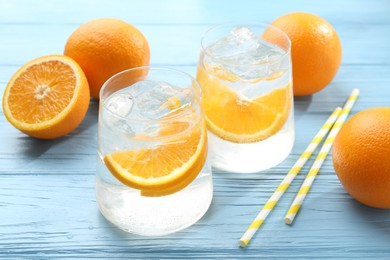 Photo of Sparkling water with orange slices in glasses, fresh fruits and straws on light blue wooden table, closeup