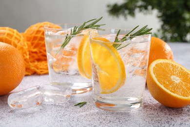 Photo of Sparkling water with orange slices and rosemary on grey table, closeup