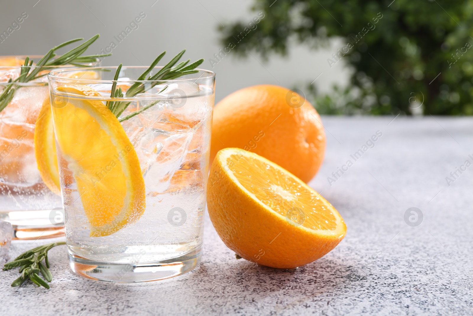 Photo of Sparkling water with orange slices and rosemary on grey table, closeup
