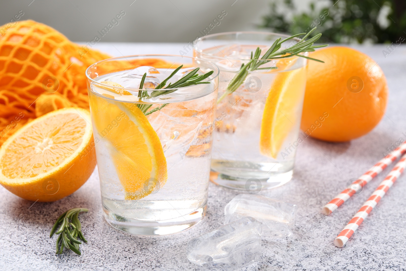 Photo of Sparkling water with orange slices and rosemary on grey table, closeup