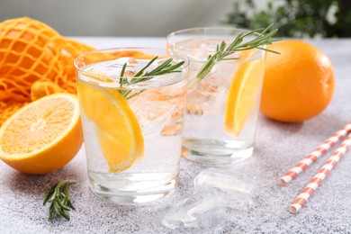 Photo of Sparkling water with orange slices and rosemary on grey table, closeup