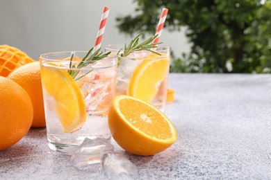 Photo of Sparkling water with orange slices and rosemary on grey table, closeup