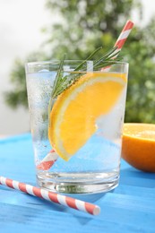 Photo of Refreshing soda water with orange slice and rosemary in glass on light blue wooden table, closeup