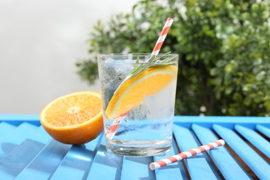 Photo of Refreshing soda water with orange slice and rosemary in glass on light blue wooden table, closeup