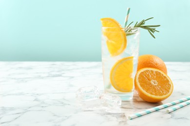 Photo of Refreshing soda drink with orange slices and rosemary in glass on white marble table. Space for text