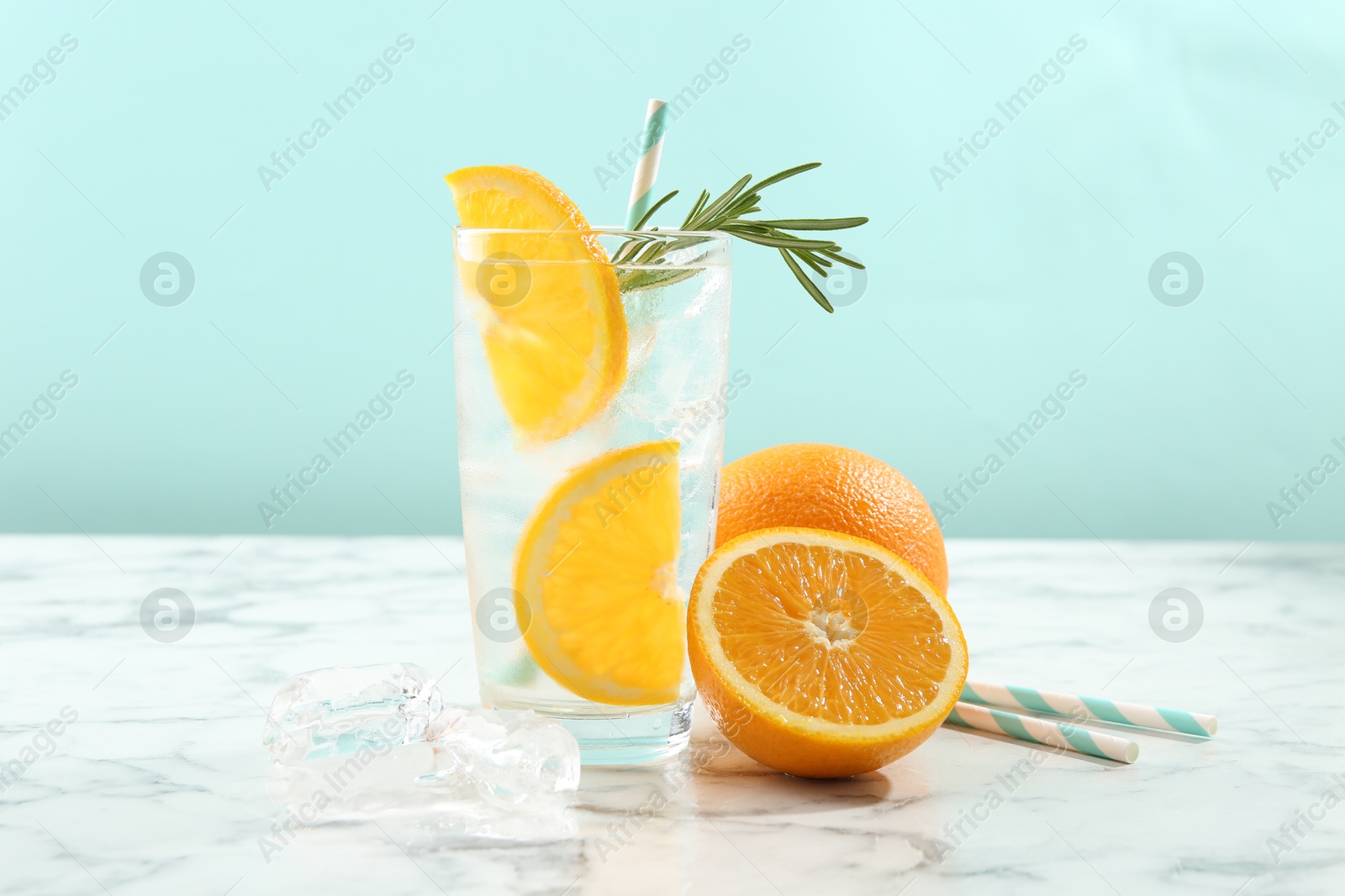 Photo of Refreshing soda drink with orange slices and rosemary in glass on white marble table