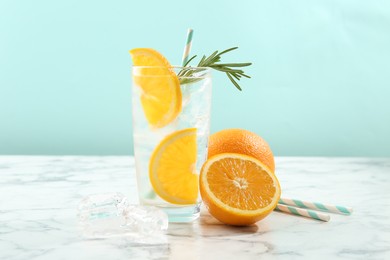 Photo of Refreshing soda drink with orange slices and rosemary in glass on white marble table