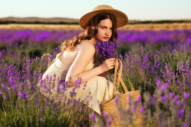 Photo of Beautiful young woman with lavender flowers and wicker bag in field