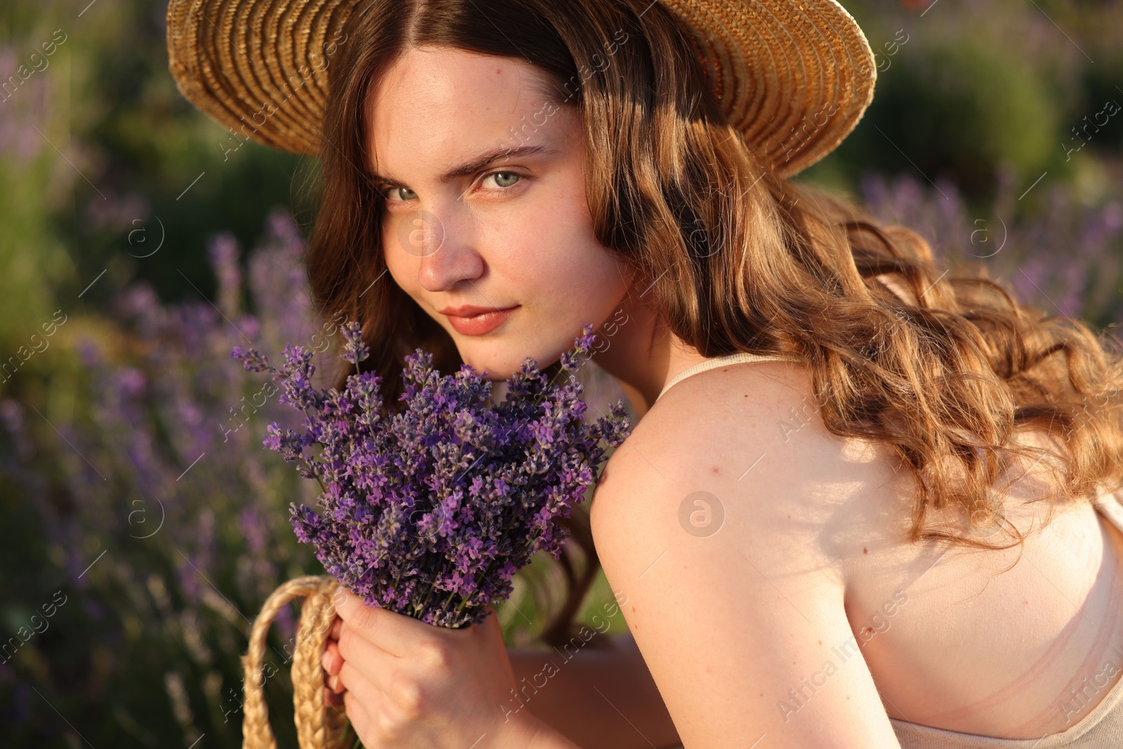 Photo of Beautiful young woman with lavender flowers in field, closeup