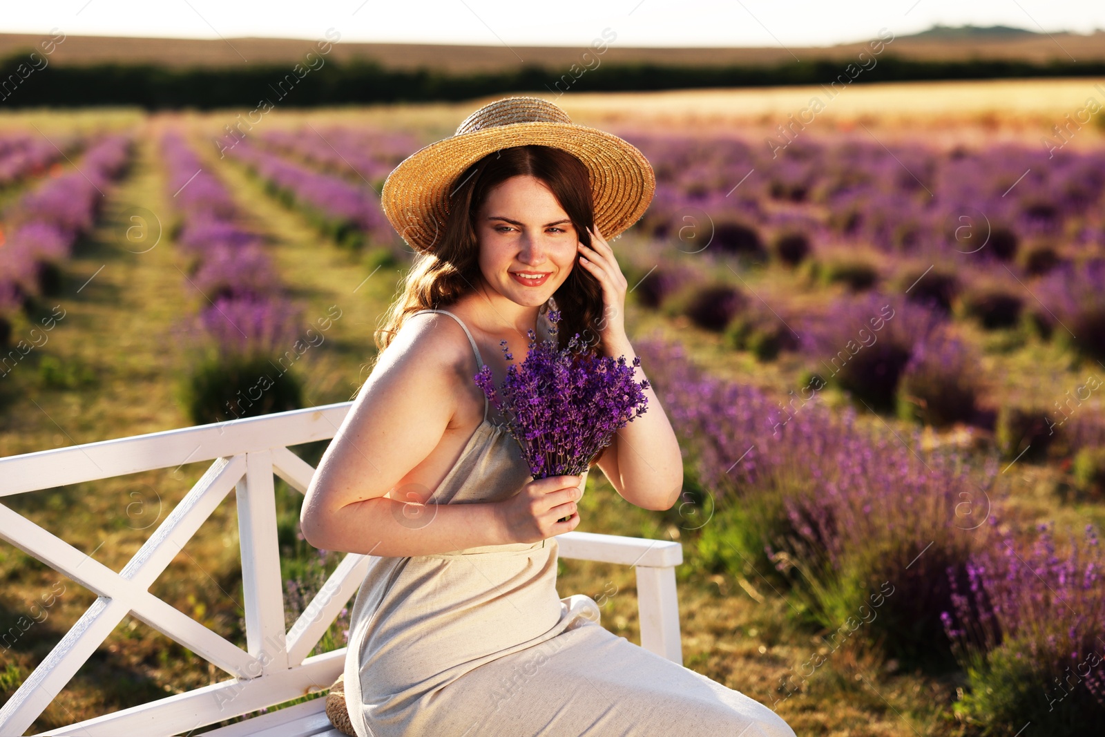 Beautiful young woman with lavender flowers on bench in field Photo of Beautiful young woman with lavender flowers on bench in field