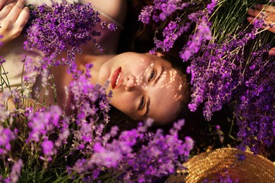 Photo of Beautiful young woman lying among lavender flowers outdoors, top view