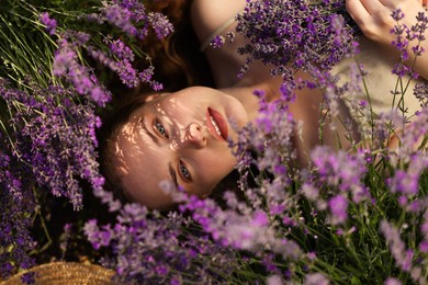 Photo of Beautiful young woman lying among lavender flowers outdoors, top view