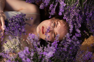 Photo of Beautiful young woman lying among lavender flowers outdoors, top view