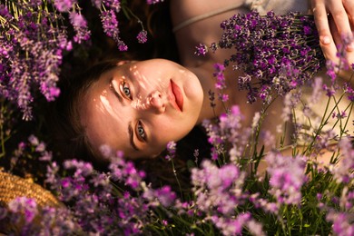 Photo of Beautiful young woman lying among lavender flowers outdoors, top view