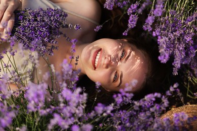 Photo of Beautiful young woman lying among lavender flowers outdoors, top view