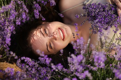 Photo of Beautiful young woman lying among lavender flowers outdoors, top view