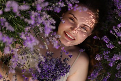 Photo of Beautiful young woman lying among lavender flowers outdoors, top view