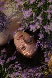 Photo of Beautiful young woman lying among lavender flowers outdoors, top view