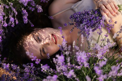 Photo of Beautiful young woman lying among lavender flowers outdoors, top view