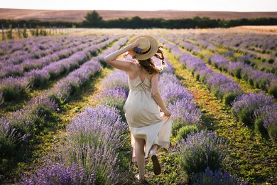 Photo of Woman with straw hat and beautiful flowers running through lavender field
